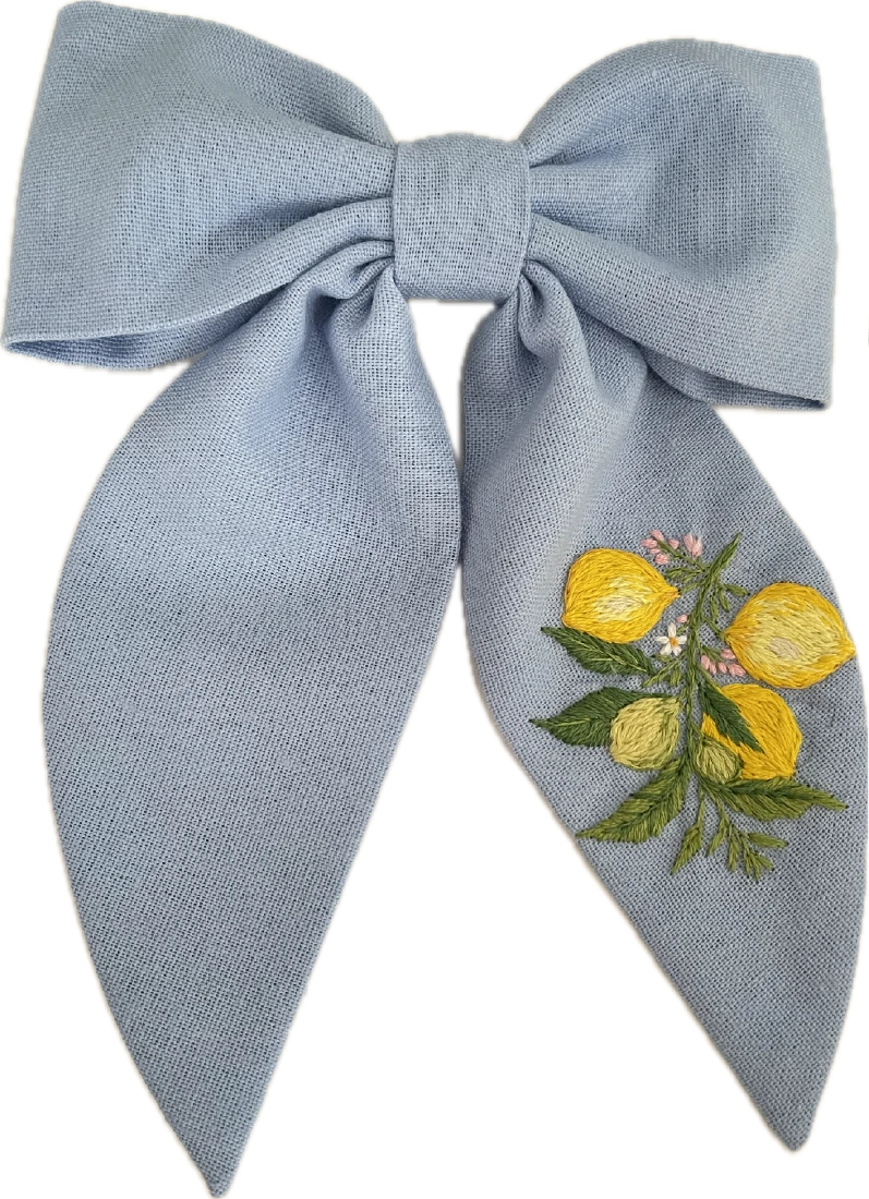 Hair bow with a metal barrette clip attached to it. The bow is made of light blue fabric and the barrette clip is used to fasten the bow to the hair.